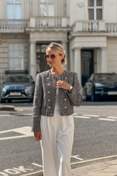 a lady wears a grey tweed jacket with white pants